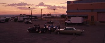 Movie still from “Flamin' Hot” (2023), directed by Eva Longoria – A group of men standing next to parked cars at sunset; Extreme Wide shot, High angle