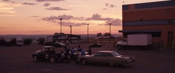Movie still from “Flamin' Hot” (2023), directed by Eva Longoria – A group of people sitting in a parking lot at sunset; Extreme Wide shot, High angle