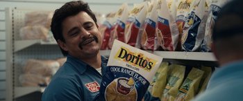 Movie still from “Flamin' Hot” (2023), directed by Eva Longoria – A man holding a bag of doritos in a store; Close Up shot, Over the shoulder angle