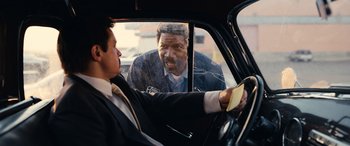 Movie still from “Flamin' Hot” (2023), directed by Eva Longoria – A man in a suit and tie driving in a car; Medium shot, Over the shoulder angle