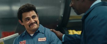 Movie still from “Flamin' Hot” (2023), directed by Eva Longoria – A man in a blue work shirt is being hugged by another man in a blue work shirt; Close Up shot, Over the shoulder angle