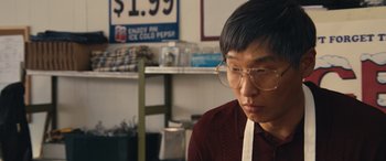 Movie still from “Flamin' Hot” (2023), directed by Eva Longoria – A man wearing glasses sitting in front of a sign; Close Up shot, Over the shoulder angle