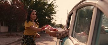 Movie still from “Flamin' Hot” (2023), directed by Eva Longoria – A woman is handing food to a man in the back of a car; Medium shot, Over the shoulder angle