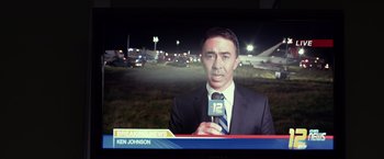 Movie still from “Flight” (2012), directed by Robert Zemeckis – A man in a suit and tie holding a microphone; Medium shot, Over the shoulder angle