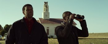 Movie still from “Flight” (2012), directed by Robert Zemeckis – Two men standing in front of a building looking through binoculars; Medium shot, Low angle