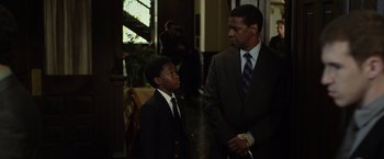 Movie still from “Flight” (2012), directed by Robert Zemeckis – A man in a suit and tie standing next to a boy in a suit; Medium shot, Over the shoulder angle