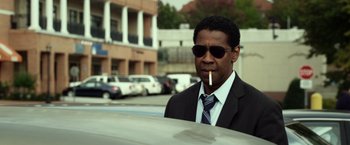 Movie still from “Flight” (2012), directed by Robert Zemeckis – A man in a suit and sunglasses smoking a cigarette in a parking lot; Medium shot, Low angle
