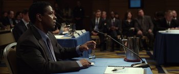 Movie still from “Flight” (2012), directed by Robert Zemeckis – A man in a business suit is holding a glass of water; Medium shot, Over the shoulder angle