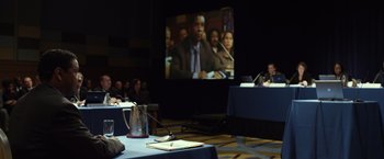 Movie still from “Flight” (2012), directed by Robert Zemeckis – A man is on a screen in front of a crowd of onlookers; Medium shot, Over the shoulder angle