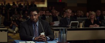 Movie still from “Flight” (2012), directed by Robert Zemeckis – A man sitting at a table in front of a microphone; Close Up shot, Over the shoulder angle