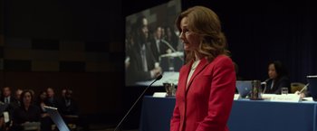 Movie still from “Flight” (2012), directed by Robert Zemeckis – A woman in a red suit stands in front of a microphone; Medium shot, Over the shoulder angle