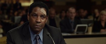 Movie still from “Flight” (2012), directed by Robert Zemeckis – A man in a suit and tie in front of a microphone; Close Up shot, Over the shoulder angle
