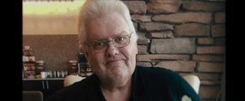 Movie still from “Flight/Risk” (2022), directed by Karim Amer – An older man with white hair wearing glasses; Close Up shot, Low angle