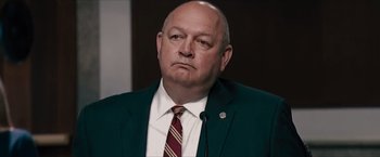 Movie still from “Flight/Risk” (2022), directed by Karim Amer – A man in a green jacket and a red tie; Close Up shot, Low angle