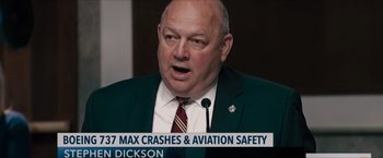 Movie still from “Flight/Risk” (2022), directed by Karim Amer – A person wearing a suit and tie; Close Up shot, Low angle