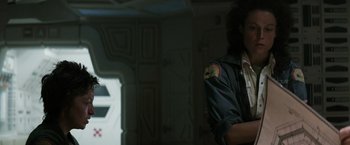 Movie still from “Alien” (1979), directed by Ridley Scott – A man standing in a dark room with his arms crossed; Medium shot, Over the shoulder angle
