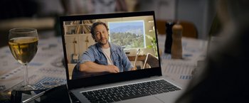 Movie still from “Flora and Son” (2023), directed by John Carney – A man sitting in front of a laptop computer on a desk; Medium shot, High angle