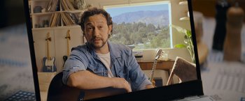 Movie still from “Flora and Son” (2023), directed by John Carney – A man sitting in front of a piano in a room with mountains in the background; Close Up shot, High angle