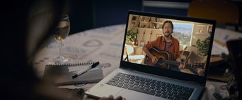 Movie still from “Flora and Son” (2023), directed by John Carney – A man sitting in front of an open laptop computer on top of a desk; Extreme Close Up shot, Overhead angle