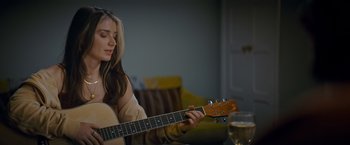 Movie still from “Flora and Son” (2023), directed by John Carney – A woman is playing a guitar while sitting in a chair; Close Up shot, Over the shoulder angle