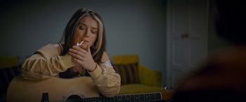 Movie still from “Flora and Son” (2023), directed by John Carney – A woman smoking a cigarette while sitting on a guitar; Medium shot, Over the shoulder angle