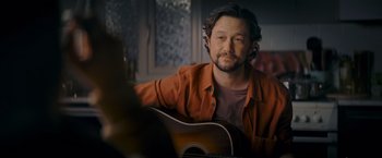 Movie still from “Flora and Son” (2023), directed by John Carney – A man sitting in front of an acoustic guitar; Close Up shot, Over the shoulder angle