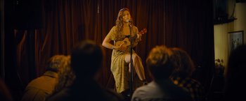Movie still from “Flora and Son” (2023), directed by John Carney – A woman in a yellow dress is playing a ukulele; Wide shot, Over the shoulder angle