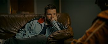 Movie still from “Flora and Son” (2023), directed by John Carney – A man sitting in a chair with his hand under his chin; Close Up shot, High angle