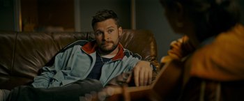 Movie still from “Flora and Son” (2023), directed by John Carney – A man sitting in a chair looking at the camera; Close Up shot, Over the shoulder angle