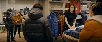 Movie still from “Flora and Son” (2023), directed by John Carney – A woman standing in front of a rack of jackets; Medium shot, Over the shoulder angle