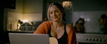 Movie still from “Flora and Son” (2023), directed by John Carney – A beautiful young lady sitting in front of a laptop computer; Close Up shot, Over the shoulder angle