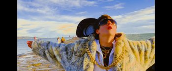 Movie still from “Flora and Son” (2023), directed by John Carney – A woman wearing a hat , sunglasses , and a fur coat on the beach; Medium shot, Low angle