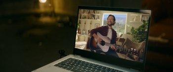Movie still from “Flora and Son” (2023), directed by John Carney – A man is playing a guitar on a laptop screen; Medium shot, Over the shoulder angle