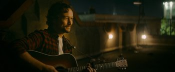 Movie still from “Flora and Son” (2023), directed by John Carney – A man holding a guitar in front of a building; Close Up shot, Over the shoulder angle