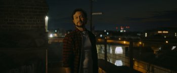 Movie still from “Flora and Son” (2023), directed by John Carney – A man standing on top of a building at night; Medium shot, Low angle
