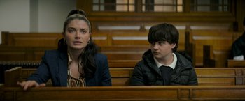 Movie still from “Flora and Son” (2023), directed by John Carney – A woman and a young boy sitting in a courtroom; Medium shot, Over the shoulder angle