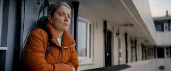 Movie still from “Flora and Son” (2023), directed by John Carney – A woman in a brown jacket standing in front of a building; Close Up shot, Low angle