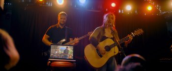 Movie still from “Flora and Son” (2023), directed by John Carney – A man and a woman are playing a song on a computer; Wide shot, Over the shoulder angle