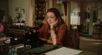Movie still from “Flora & Ulysses” (2021), directed by Lena Khan – A woman sitting at a table with her hand on her chin; Medium shot, Low angle