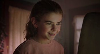Movie still from “Flora & Ulysses” (2021), directed by Lena Khan – A young girl smiling for the camera in a room; Close Up shot, Over the shoulder angle