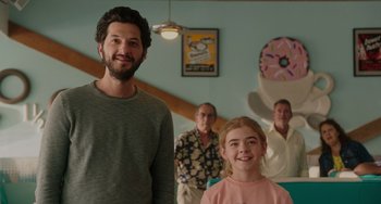 Movie still from “Flora & Ulysses” (2021), directed by Lena Khan – A man and a girl standing in front of a group of people; Medium shot, Over the shoulder angle