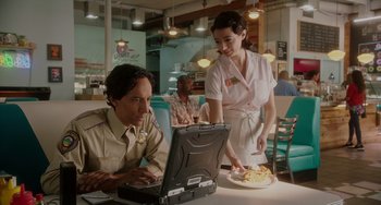 Movie still from “Flora & Ulysses” (2021), directed by Lena Khan – A man and a woman at a table with a laptop; Medium shot, Over the shoulder angle