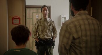 Movie still from “Flora & Ulysses” (2021), directed by Lena Khan – A man in a brown shirt is standing in front of two other men; Medium shot, Over the shoulder angle