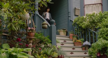 Movie still from “Flora & Ulysses” (2021), directed by Lena Khan – A woman is walking down the steps of a house; Wide shot, Low angle