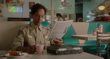 Movie still from “Flora & Ulysses” (2021), directed by Lena Khan – A man sitting at a table reading a newspaper; Medium shot, Over the shoulder angle