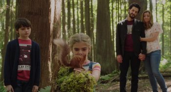 Movie still from “Flora & Ulysses” (2021), directed by Lena Khan – A young girl holding a squirrel in a forest; Medium shot, Over the shoulder angle