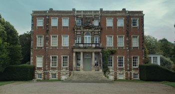 Movie still from “Flux Gourmet” (2022), directed by Peter Strickland – An old brick building with steps leading up to it; Extreme Wide shot, Low angle