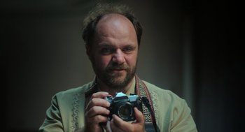 Movie still from “Flux Gourmet” (2022), directed by Peter Strickland – A man holding a camera in front of a mirror; Close Up shot, Low angle