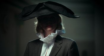 Movie still from “Flux Gourmet” (2022), directed by Peter Strickland – A woman wearing a black hat and a white shirt; Close Up shot, Low angle