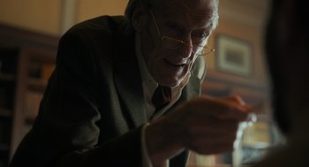 Movie still from “Flux Gourmet” (2022), directed by Peter Strickland – An older man wearing glasses and a suit; Close Up shot, Low angle